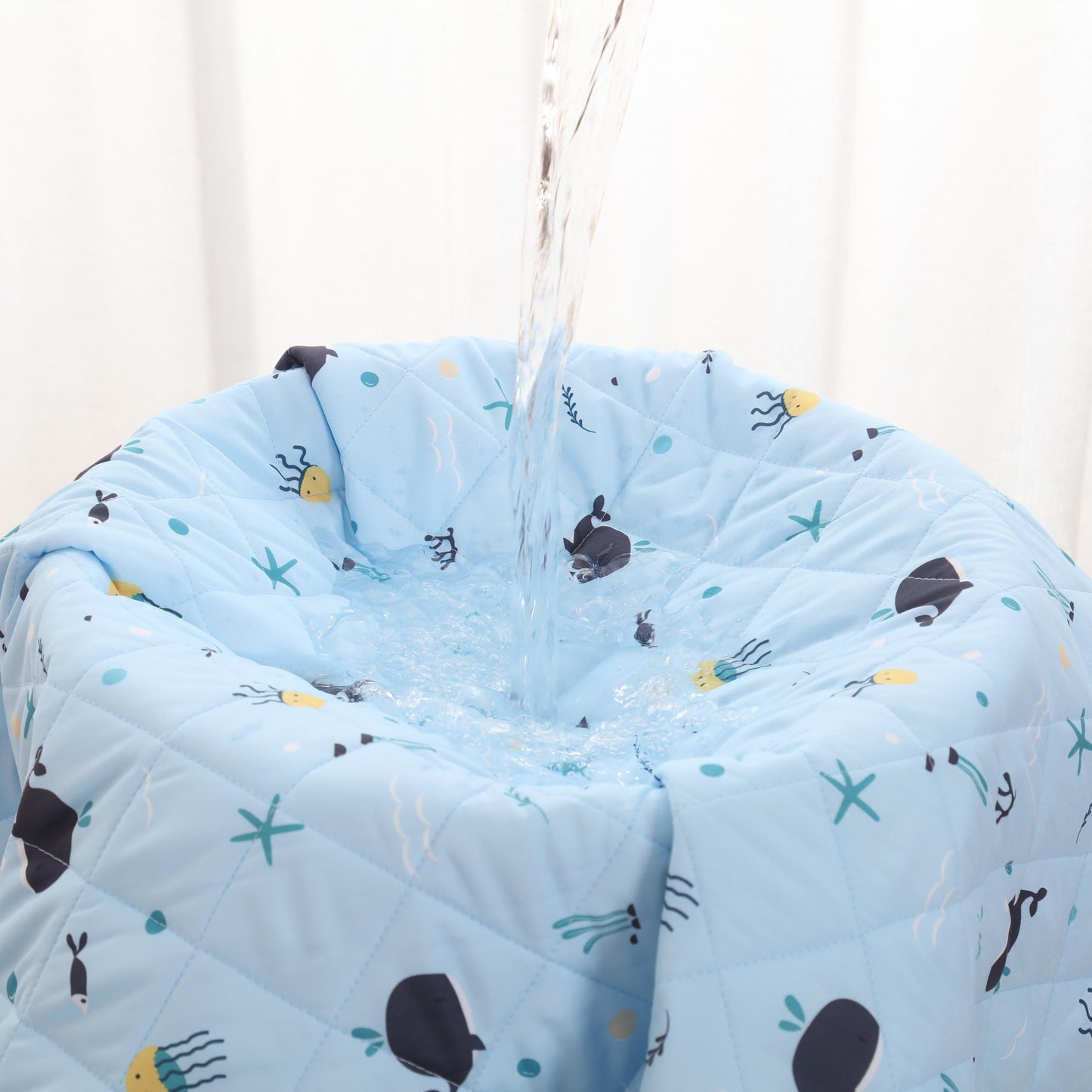 Blue quilt with whales designs hanging against a white curtain background