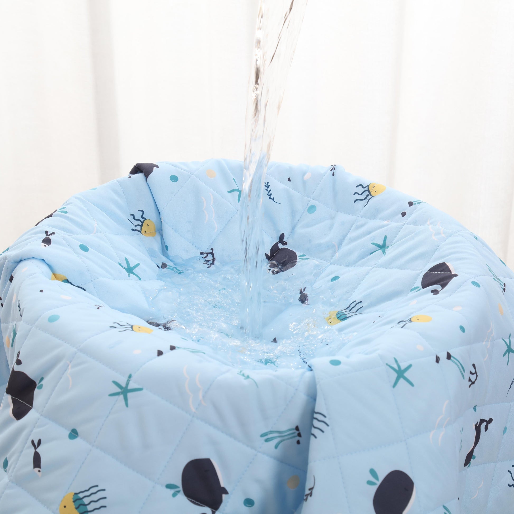 Blue quilt with whales designs hanging against a white curtain background